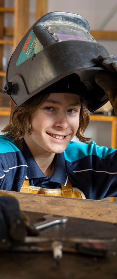 Informer Student Lifts Their Welding Helmet While Working at a Metalwork Bench