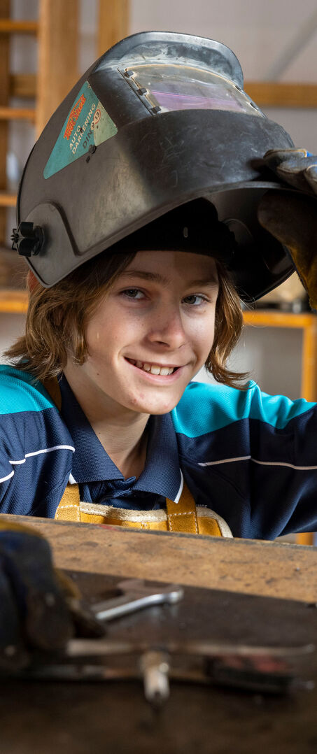 Student Lifts Their Welding Helmet While Working at a Metalwork Bench